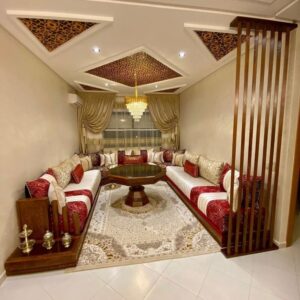 Salon marocain luxueux avec plafond sculpté, rideaux dorés et mobilier traditionnel élégant.